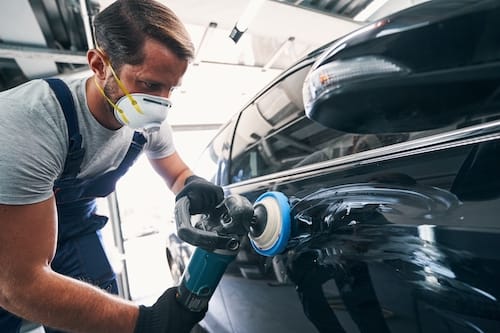 Repairman,Using,Polisher,With,Blue,Pad,On,Black,Automobile